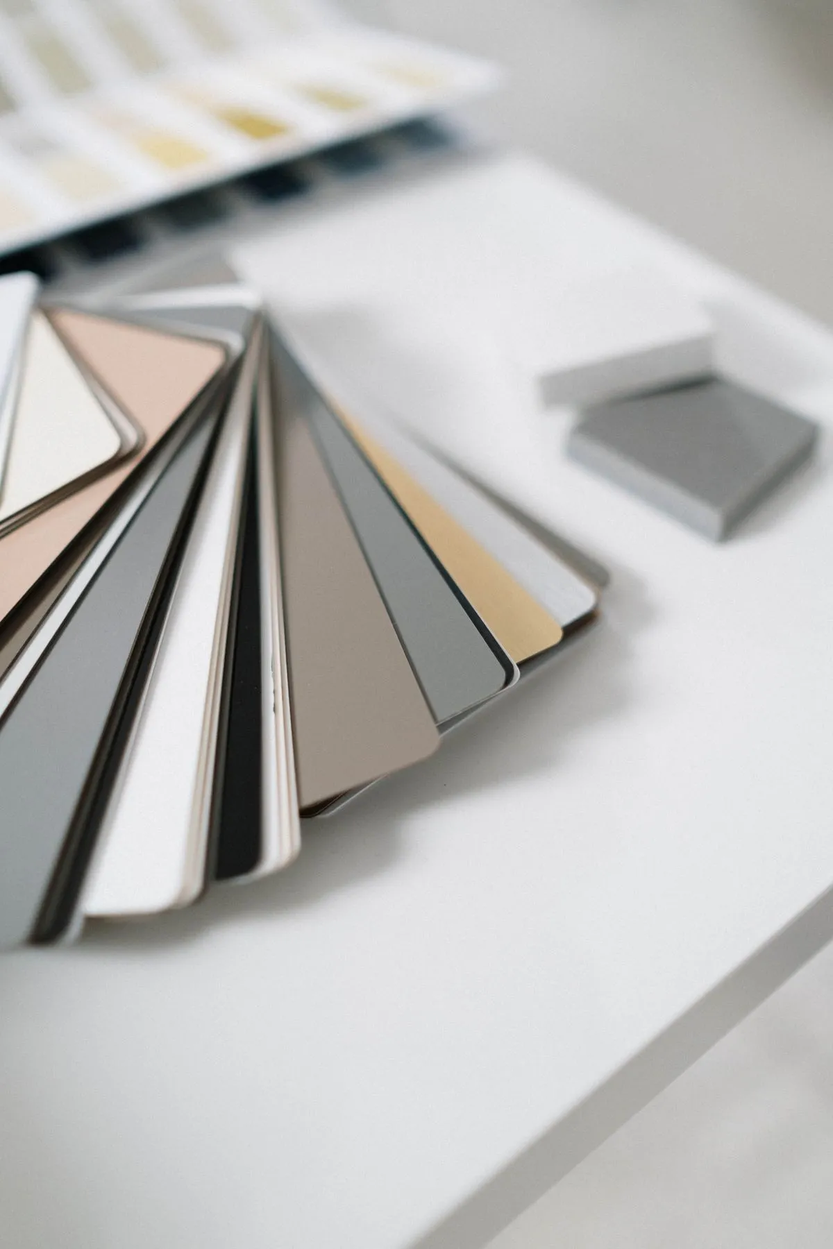 A fan of muted paint color samples arranged on a white table.