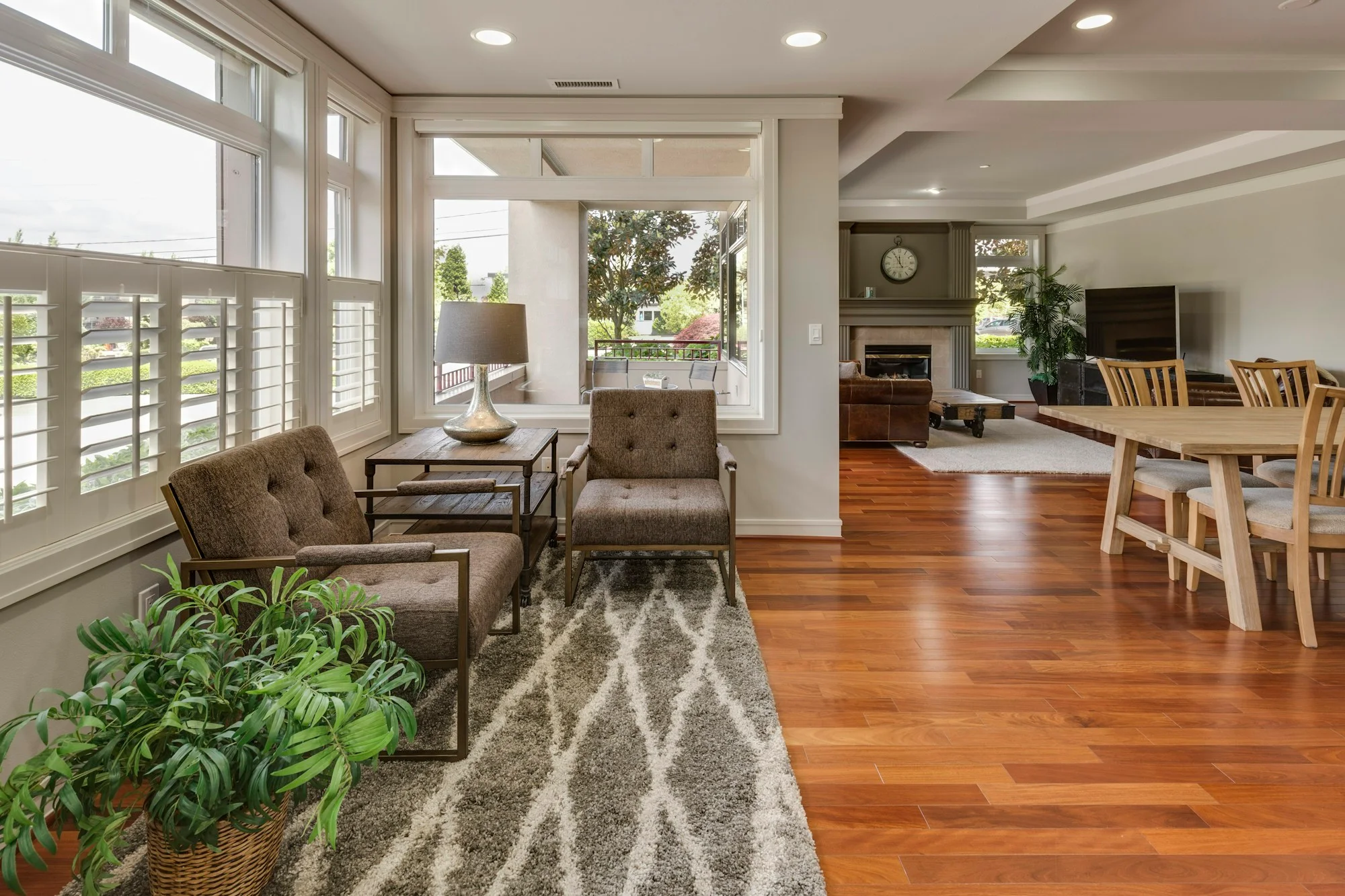 Sunlit living and dining area with upholstered chairs, natural wood floors, and greenery.