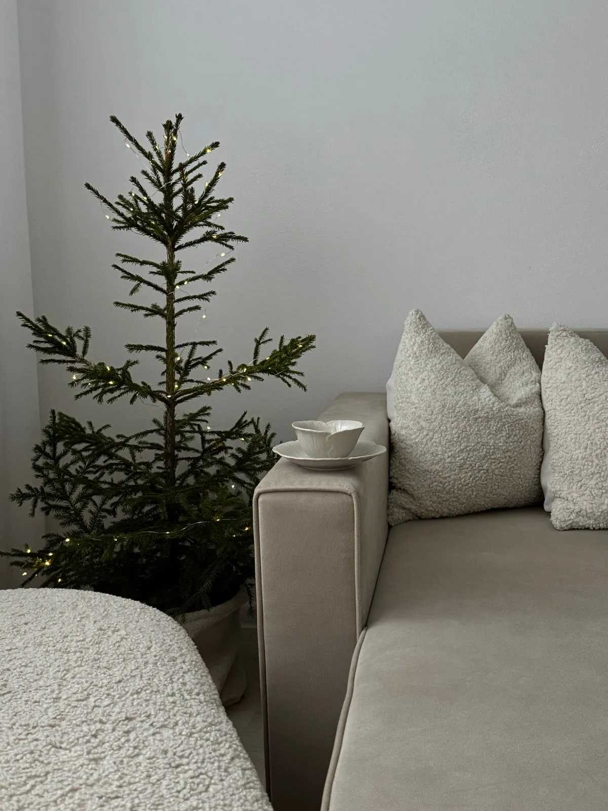 A softly lit Christmas tree beside a cream sofa with textured cushions.